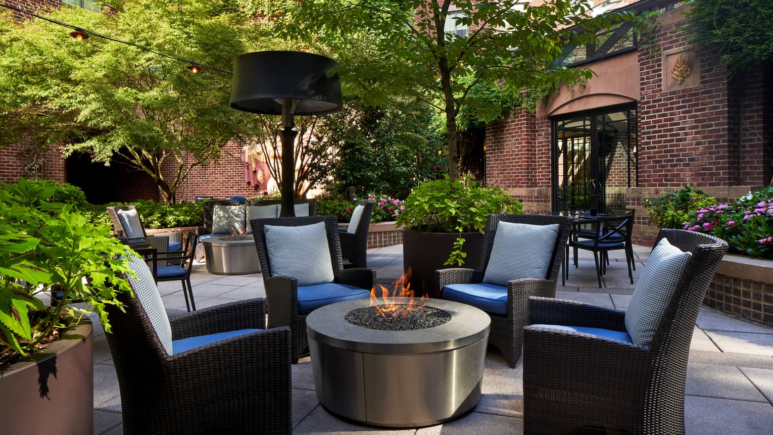 An outdoor patio area with a fire and four cushioned chairs.