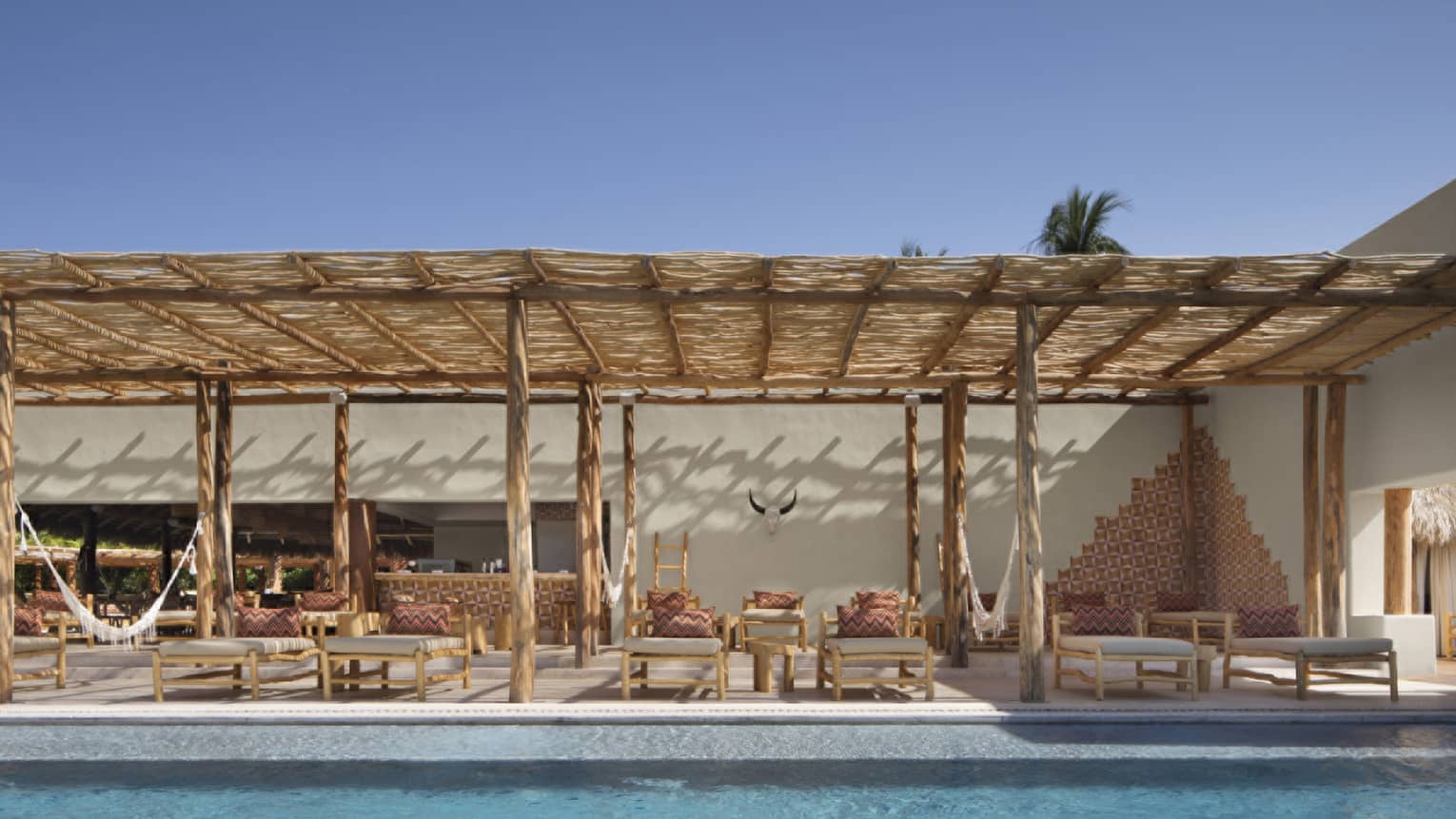 Outdoor pool with bamboo lounge chairs under thatched roof awning