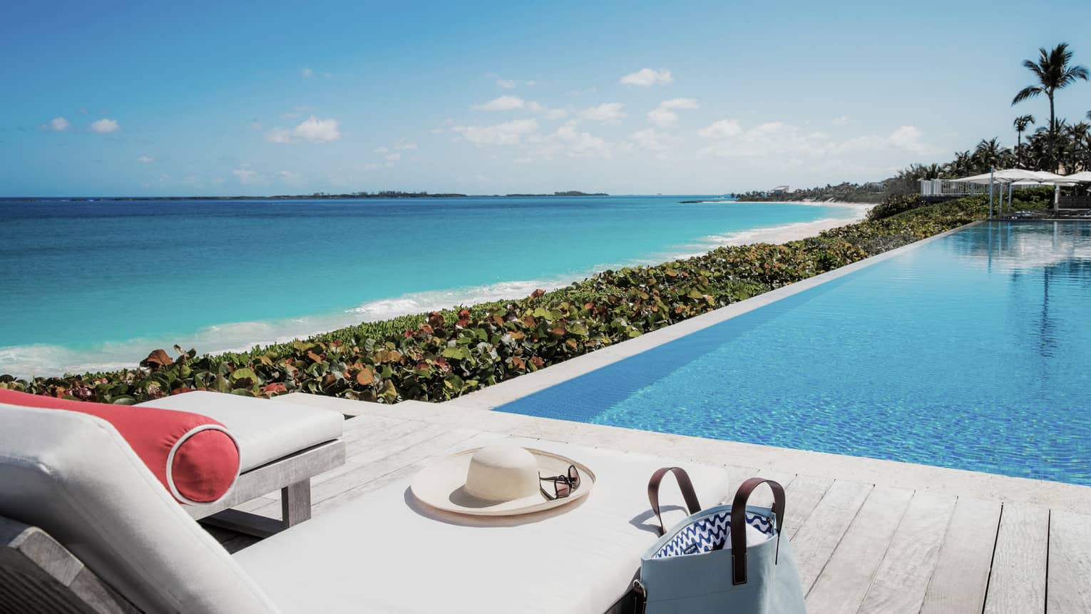 Sunhat, sunglasses, purse by lounge chair on sunny deck beside outdoor swimming pool