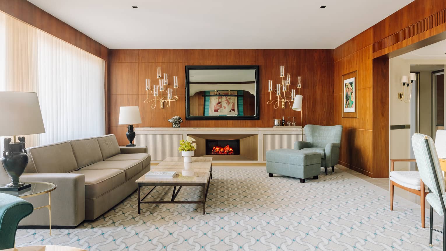 Spacious hotel living room with a sofa, armchair, fireplace, coffee table and wood-paneled walls with decorative lighting.