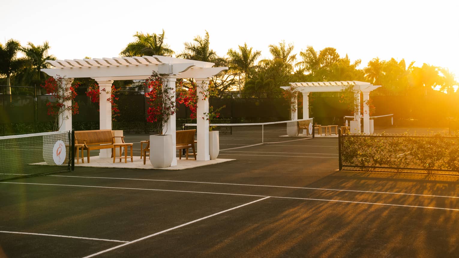 Three tennis courts with a white pergola and seating set between each court