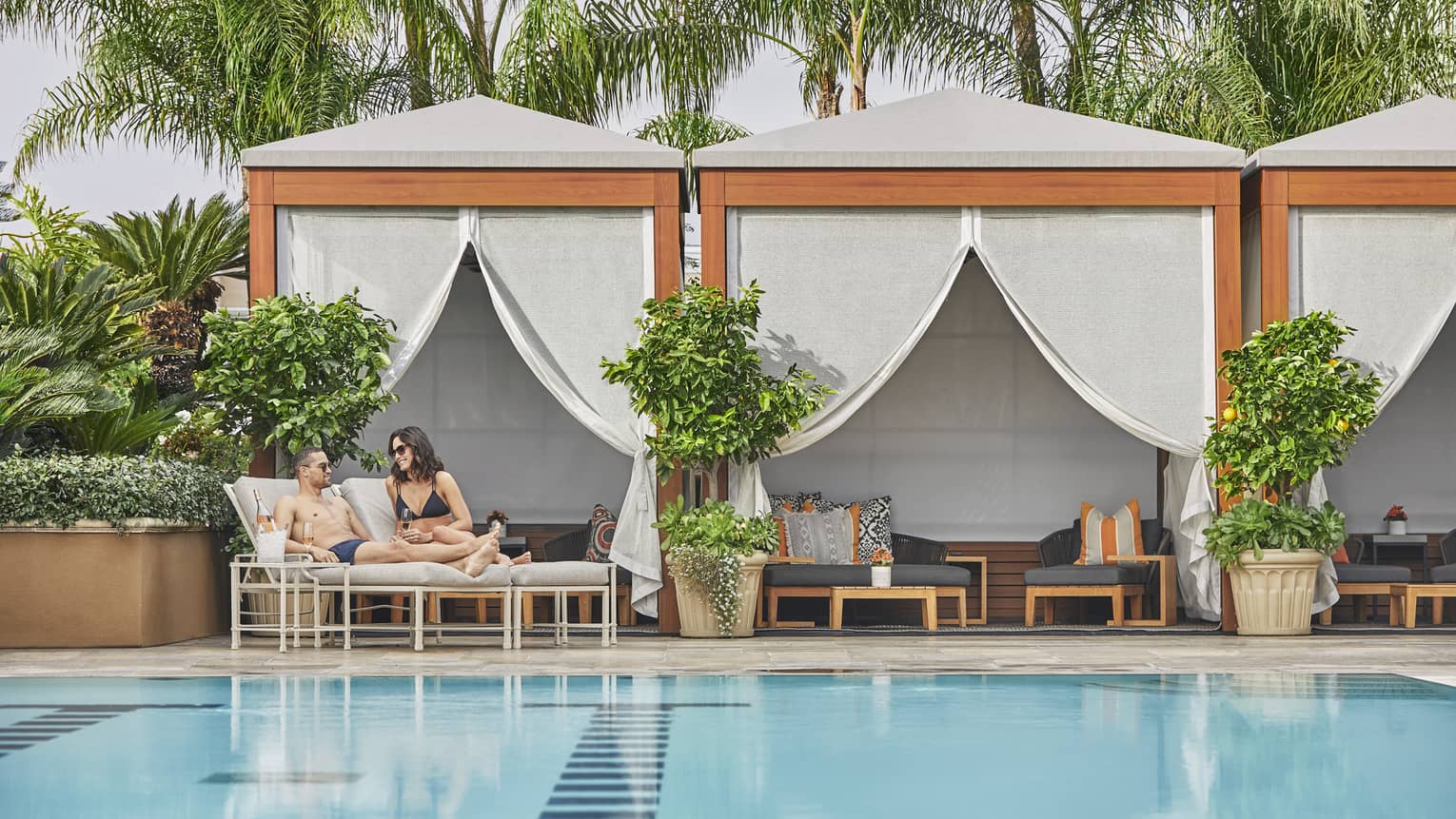 A couple sips Champagne from loungers in a cabana by the pool.