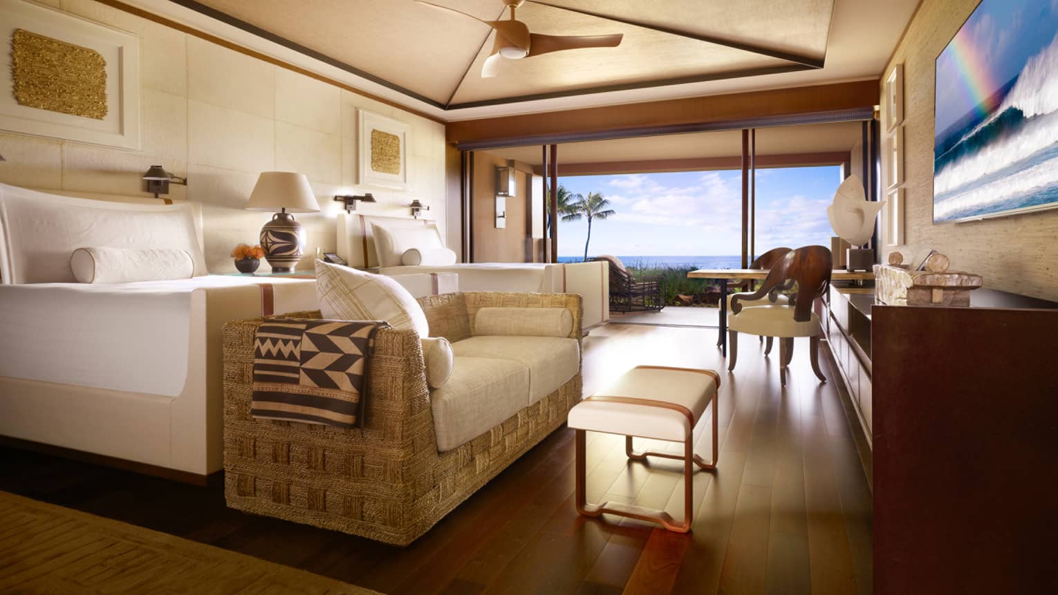 Oceanfront Room bed, wicker sofa with white cushions, bench at foot, dining table by open wall to patio