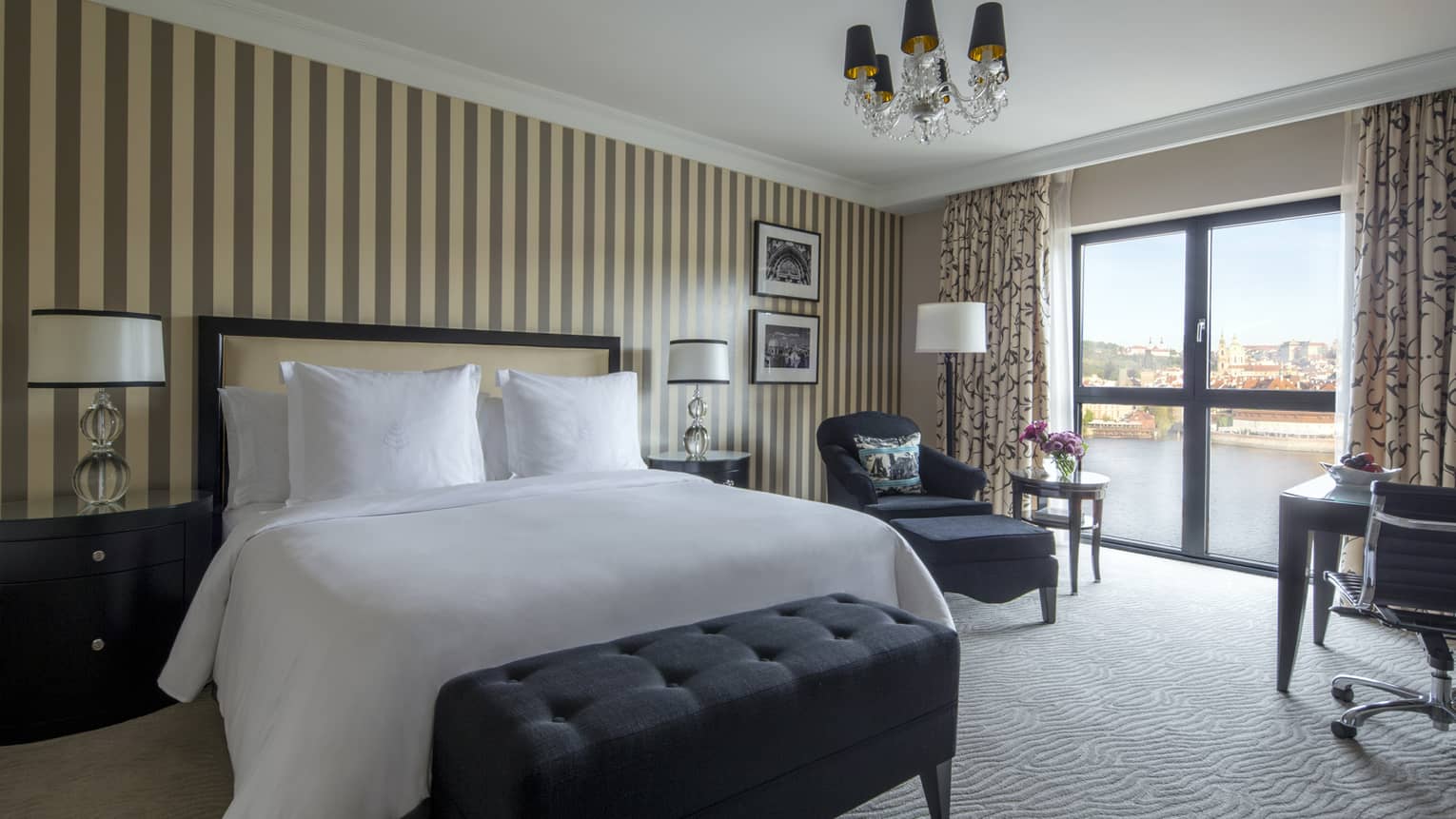 White bed flanked by side tables with mirrors against vertically striped wall, chaise in corner, river view
