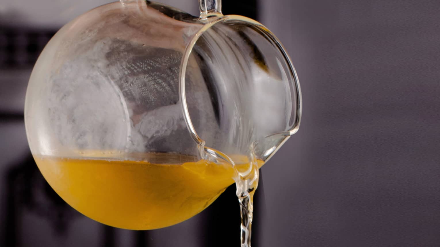 Hot tea in a glass pitcher being poured into a chilled glass dish filled with flower petals