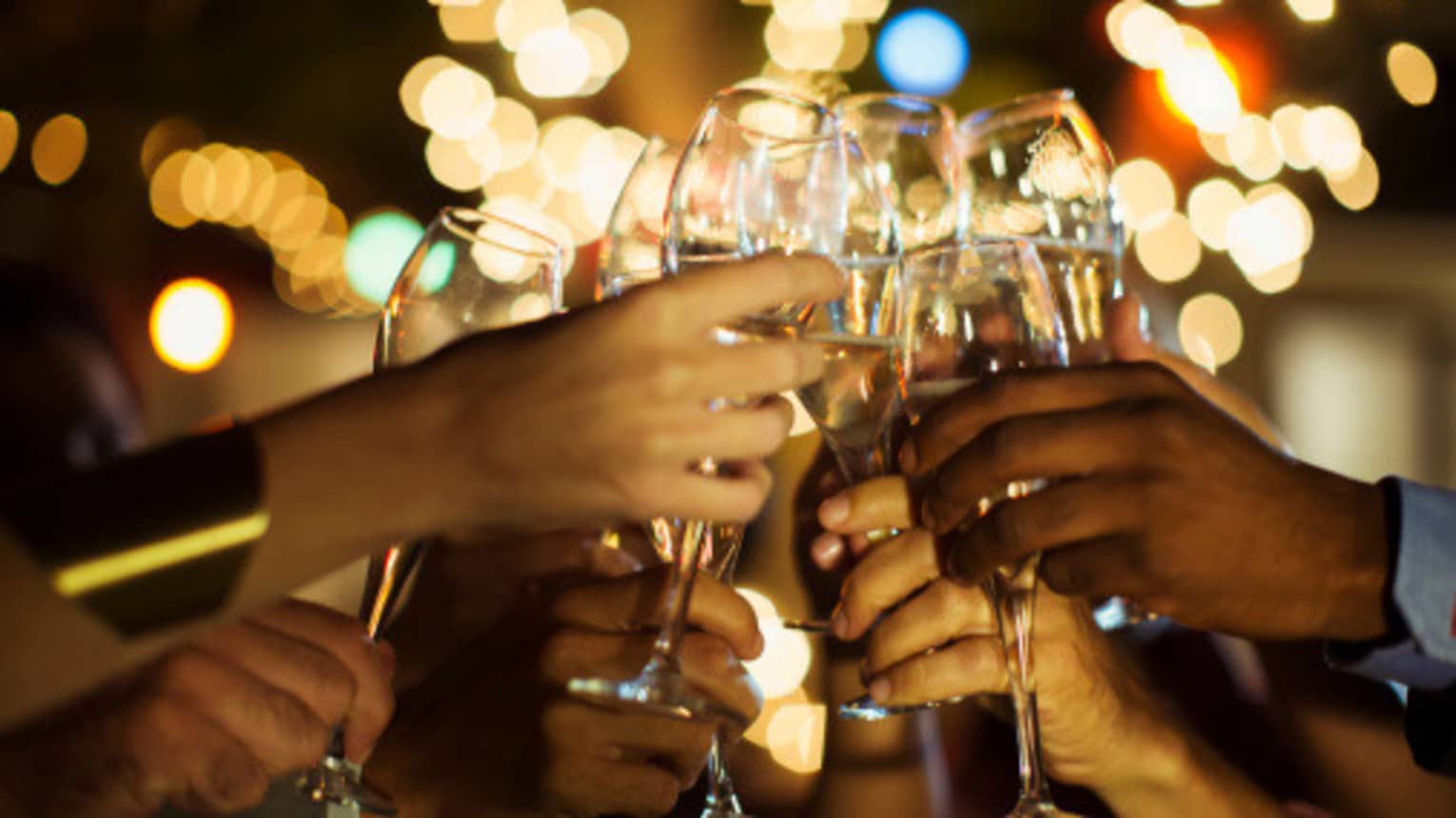 A group of guests clink their glasses of champagne together on a patio with twinkle lights