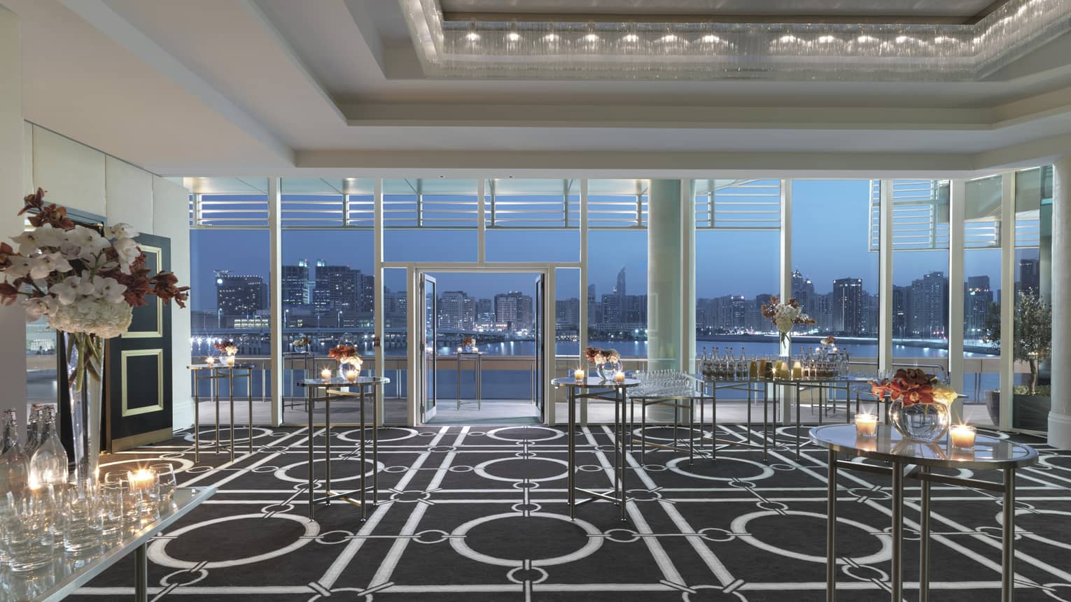 Cocktail reception tables with small candles, flowers in Liwa Ballroom, floor-to-ceiling windows with sky at dusk