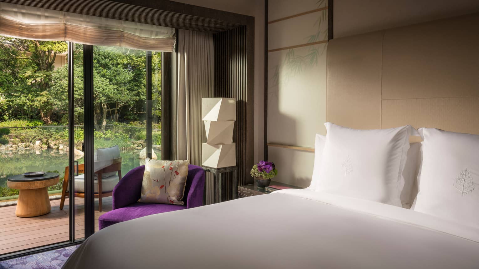 Four Seasons Executive Suite bed by bright purple armchair, modern white lantern by glass door