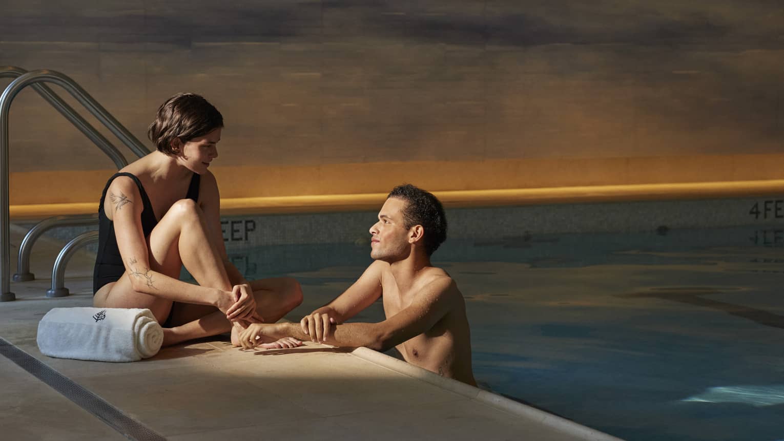Person sitting poolside with a towel talking to another person leaning on the edge of the pool at Four Seasons luxury hotel