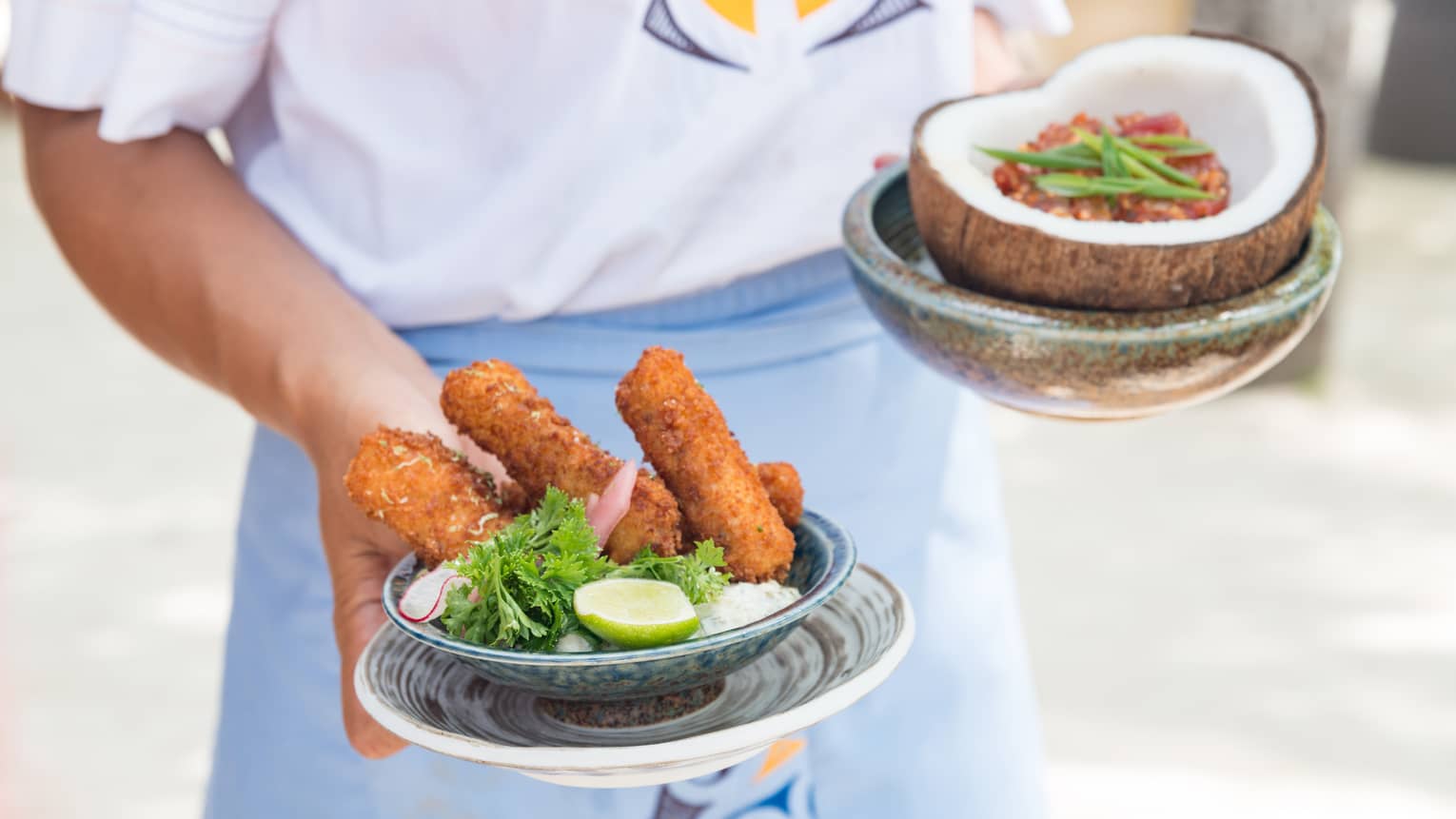 Hotel staff holds appetizers in small bowl and coconut shell