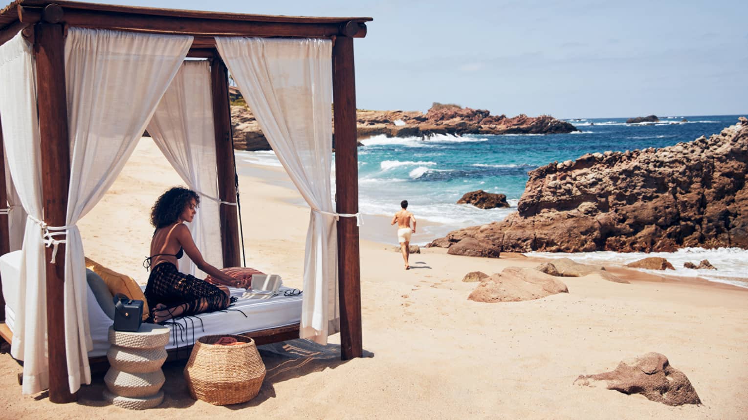 A woman on a small bed with a covering on a beach.