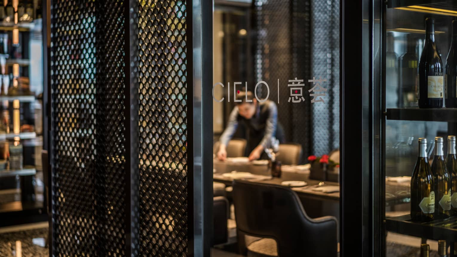 Server sets dining table behind glass wall with Cielo name, logo