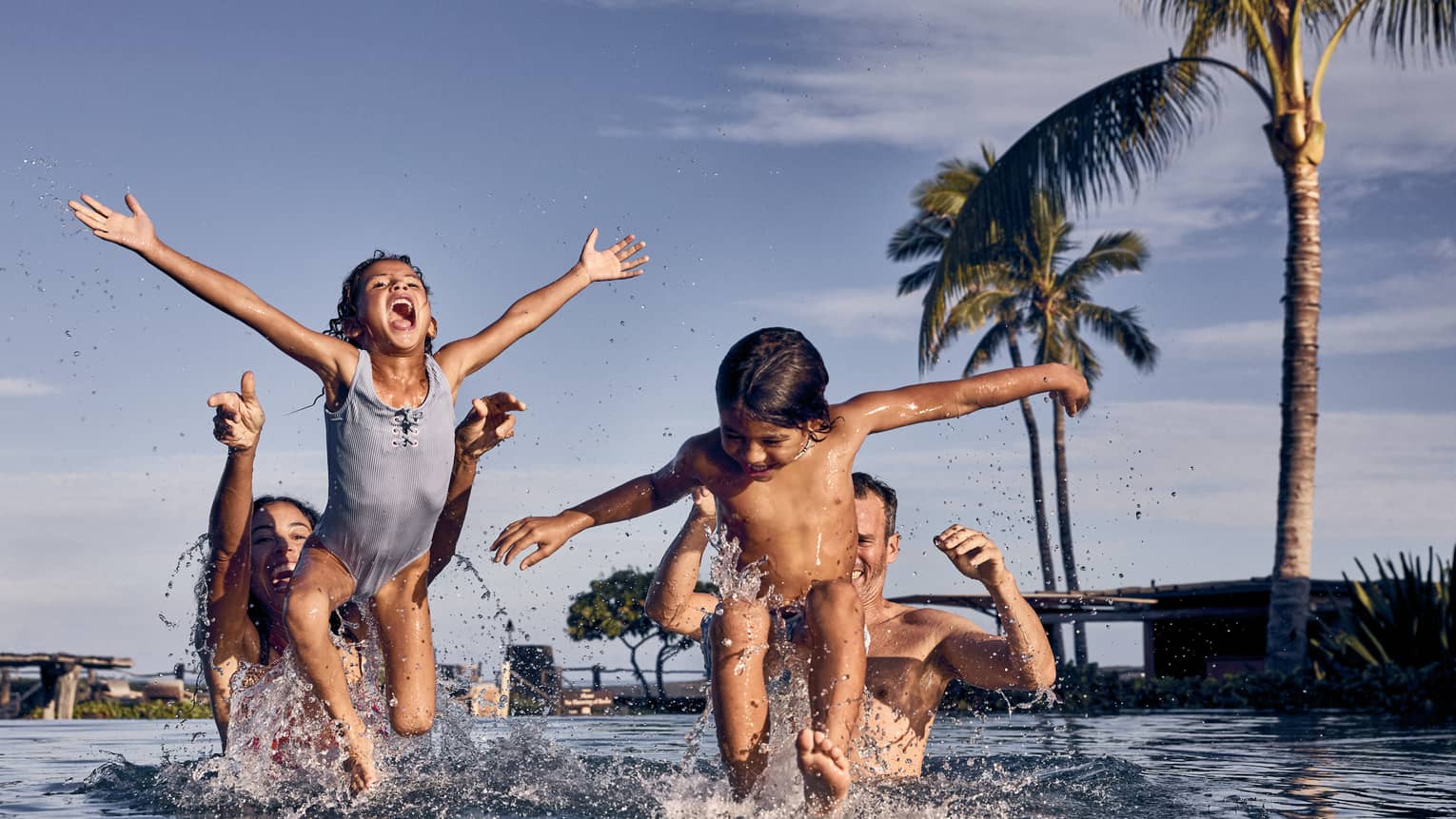 Man and woman playing throw their young children in a pool in a tropical resort setting