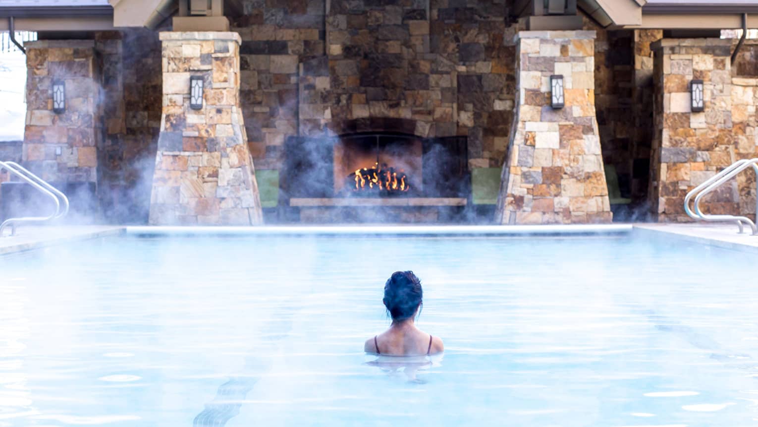 Guest standing in the heated pool, a brick building with a fireplace in the background.