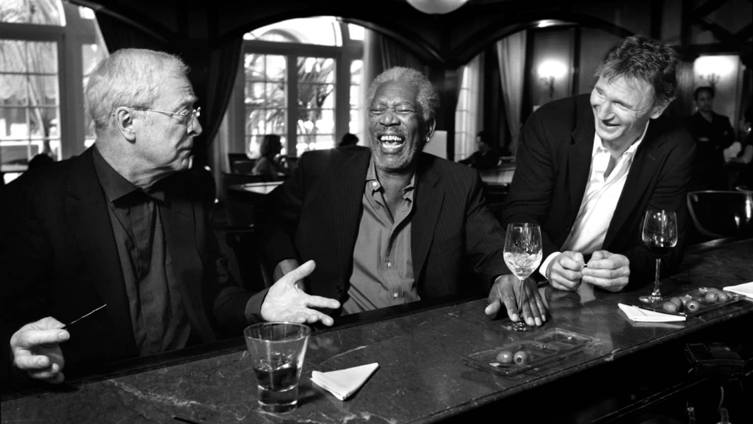 A black and white photo of three men sitting at a bar.