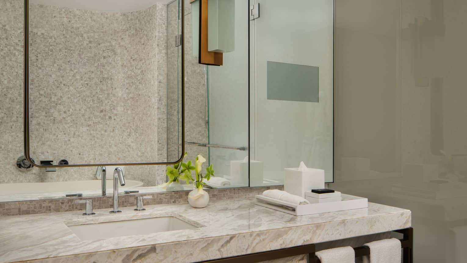 Luxury hotel bathroom vanity with marble countertop, a large mirror, a small vase with flowers, and neatly arranged toiletries