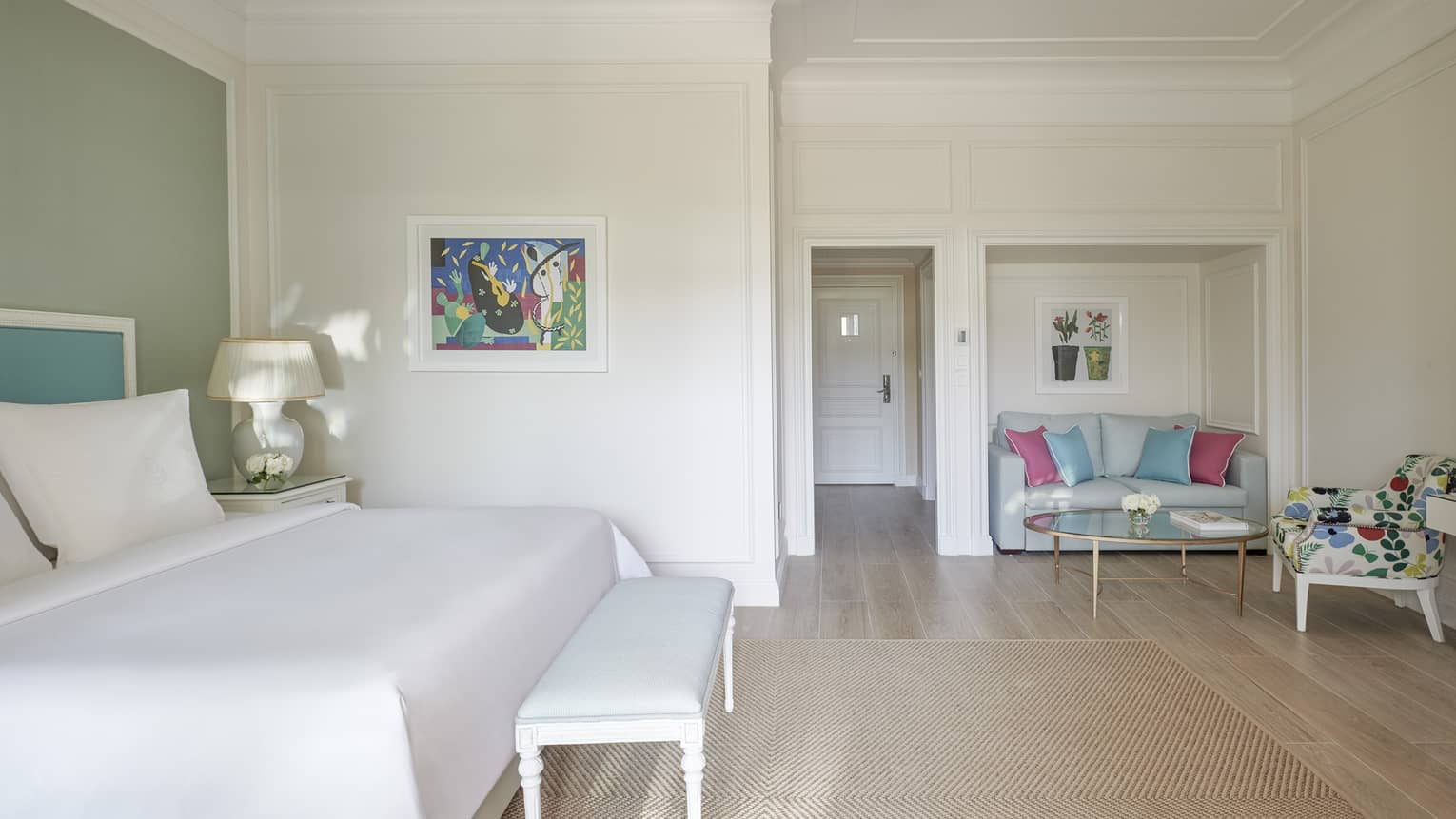 White room, white bed with blue headboard on green wall, foot bench, wood floor, seating area