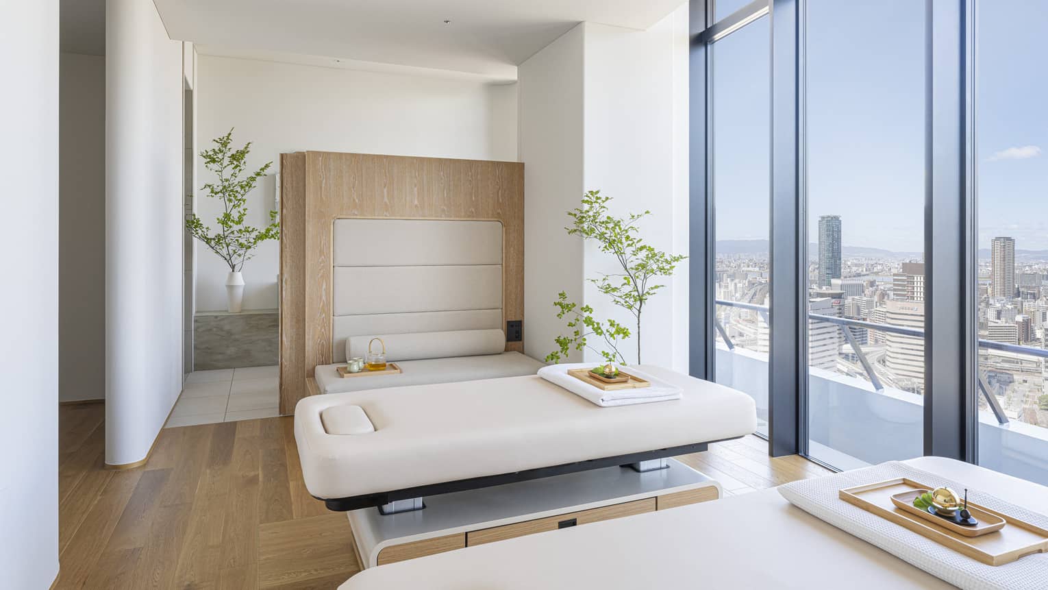 Spa treatment room with two treatment tables and wall of windows overlooking city at The Spa at Four Seasons Hotel Osaka