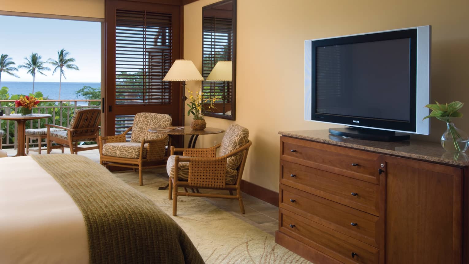 Oceanfront Room end of bed with folded wood blanket, dresser with TV, table and chairs by patio