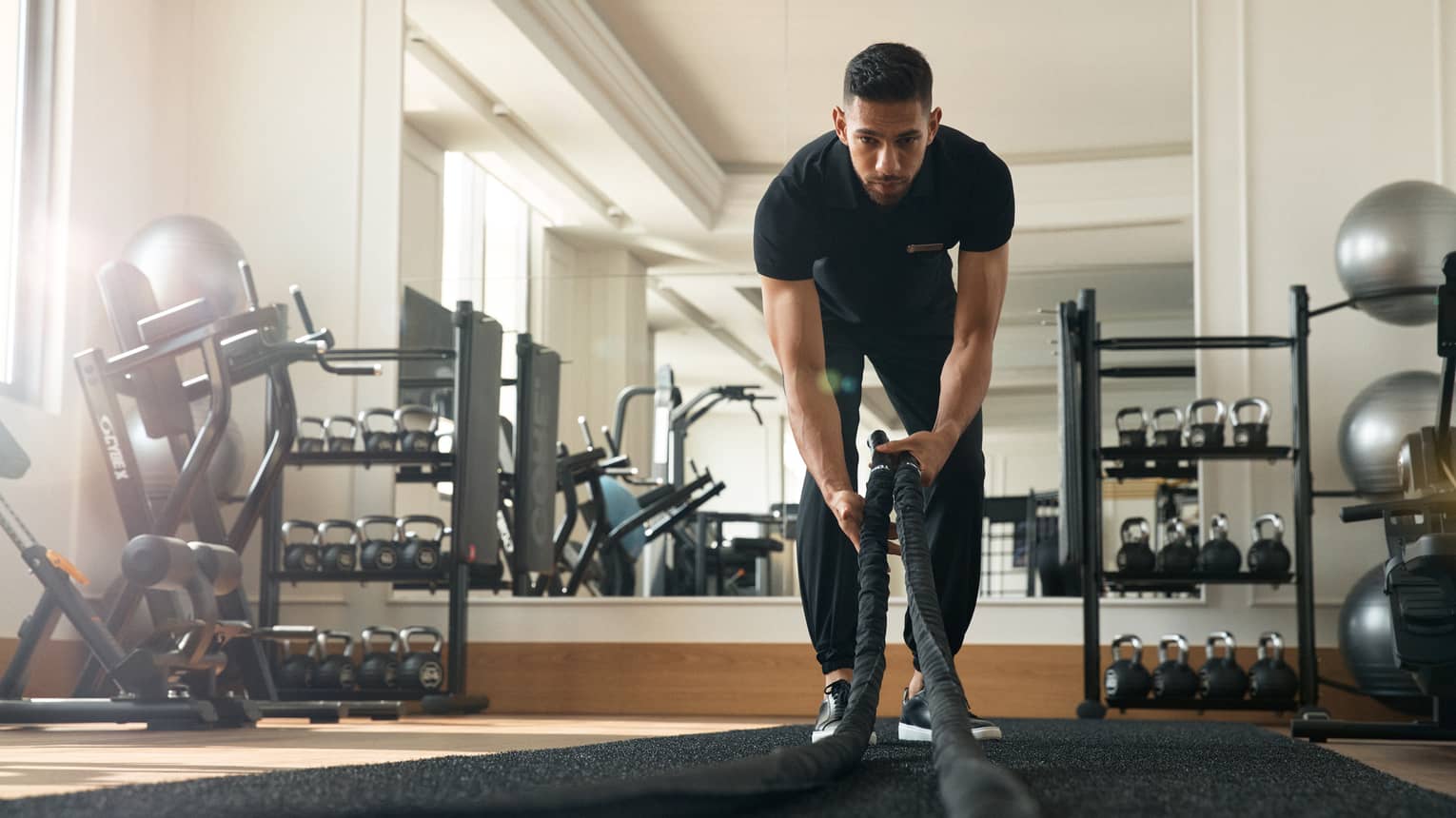Man works out in fitness room using a heavy rope