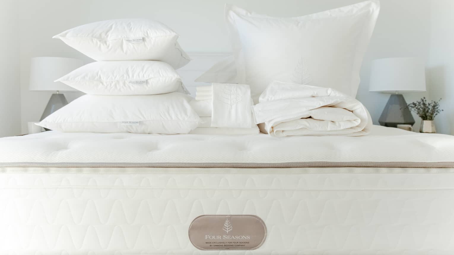 Queen bed stacked with folded white linens and feather pillows