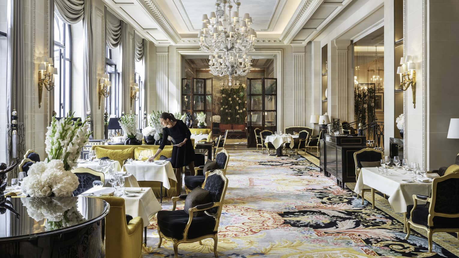 Staff member setting table in formal dining area with Queen Anne chairs, chartreuse sofas, white floral arrangements and floor-to-ceiling windows