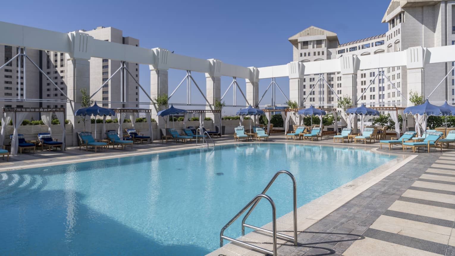 Outdoor pool surrounded by teal lounge chairs and white column