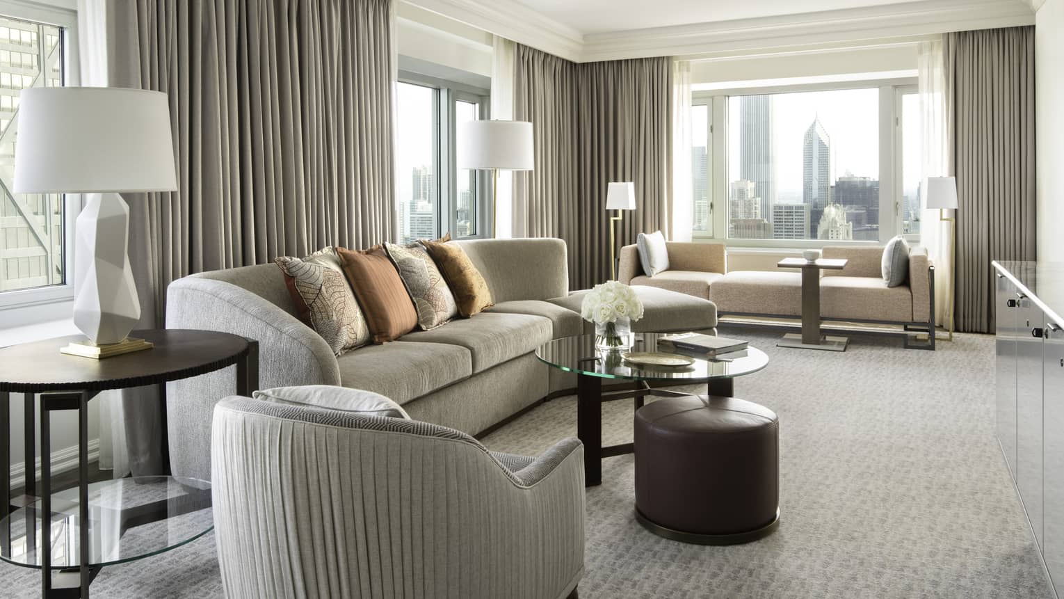 Living area with grey sofa, glass table, beige carpet, grey curtains, large windows