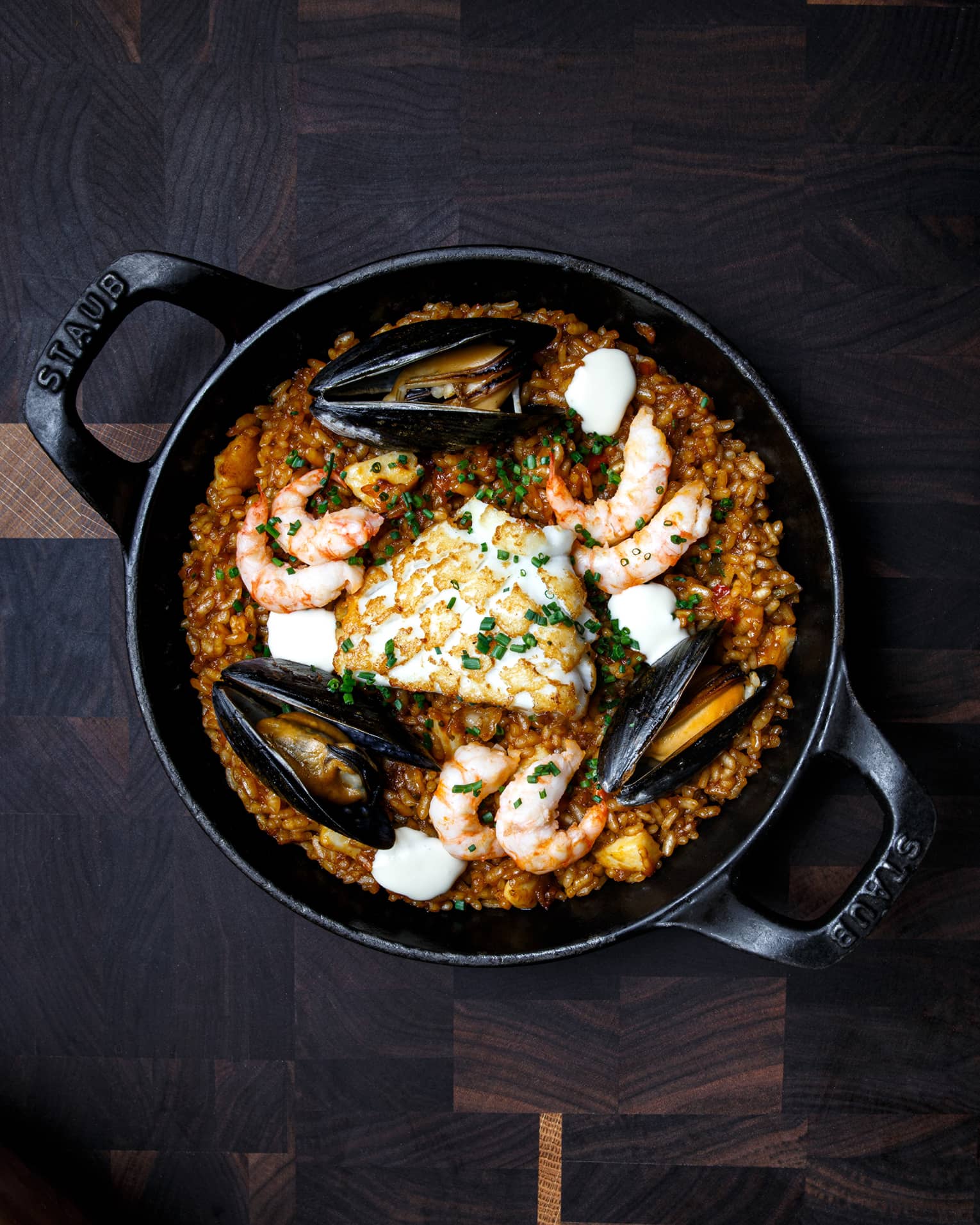 Prawns, squid and mussels on a bed of red Bomba rice in a black Staub brand cast iron skillet 
