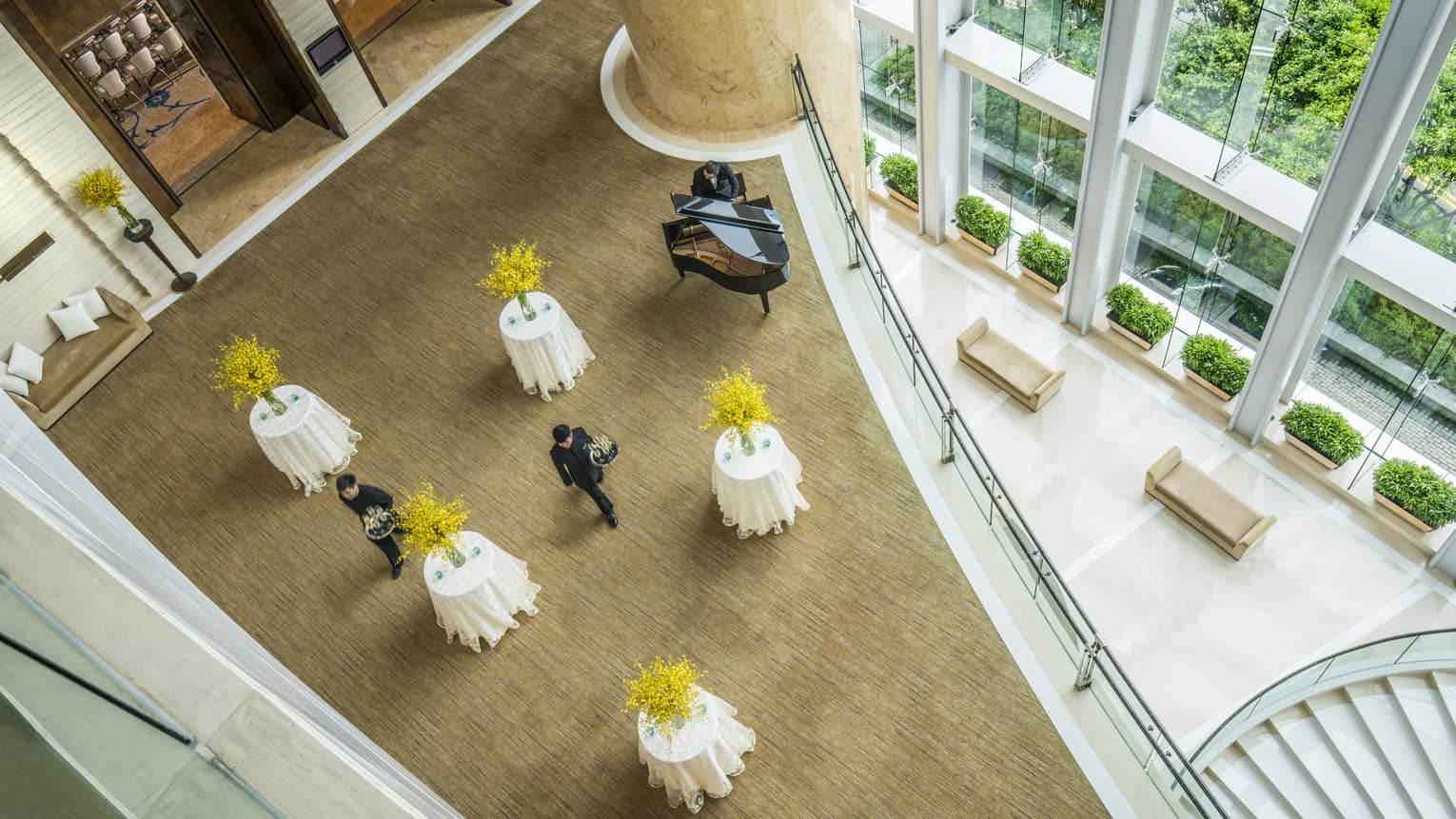 From above, a view of pre-function space set with five cocktail tables, each with yellow flowers. Two servers walk through the tables.