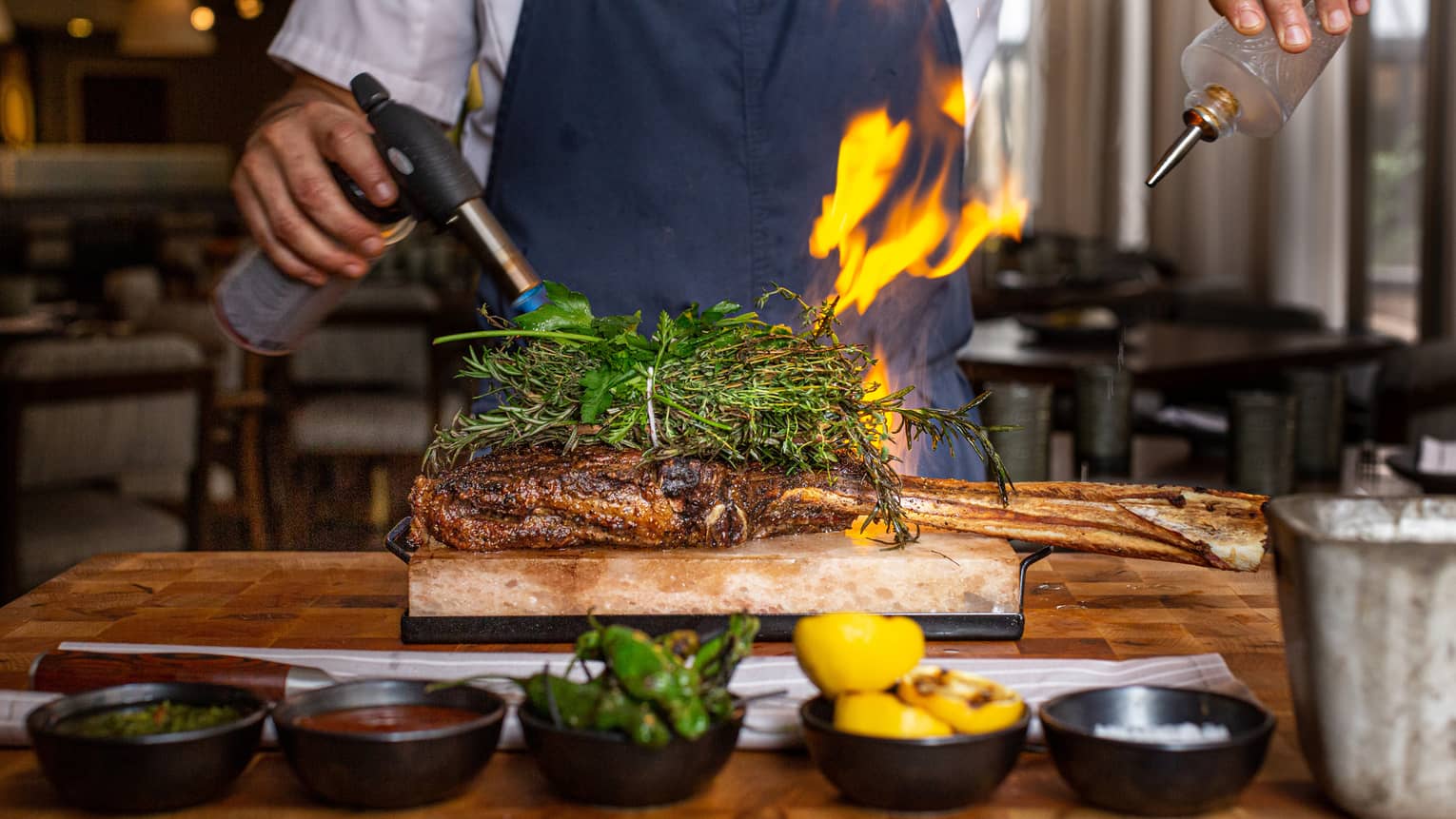 A chef using a blowtorch and oil to cook meat.