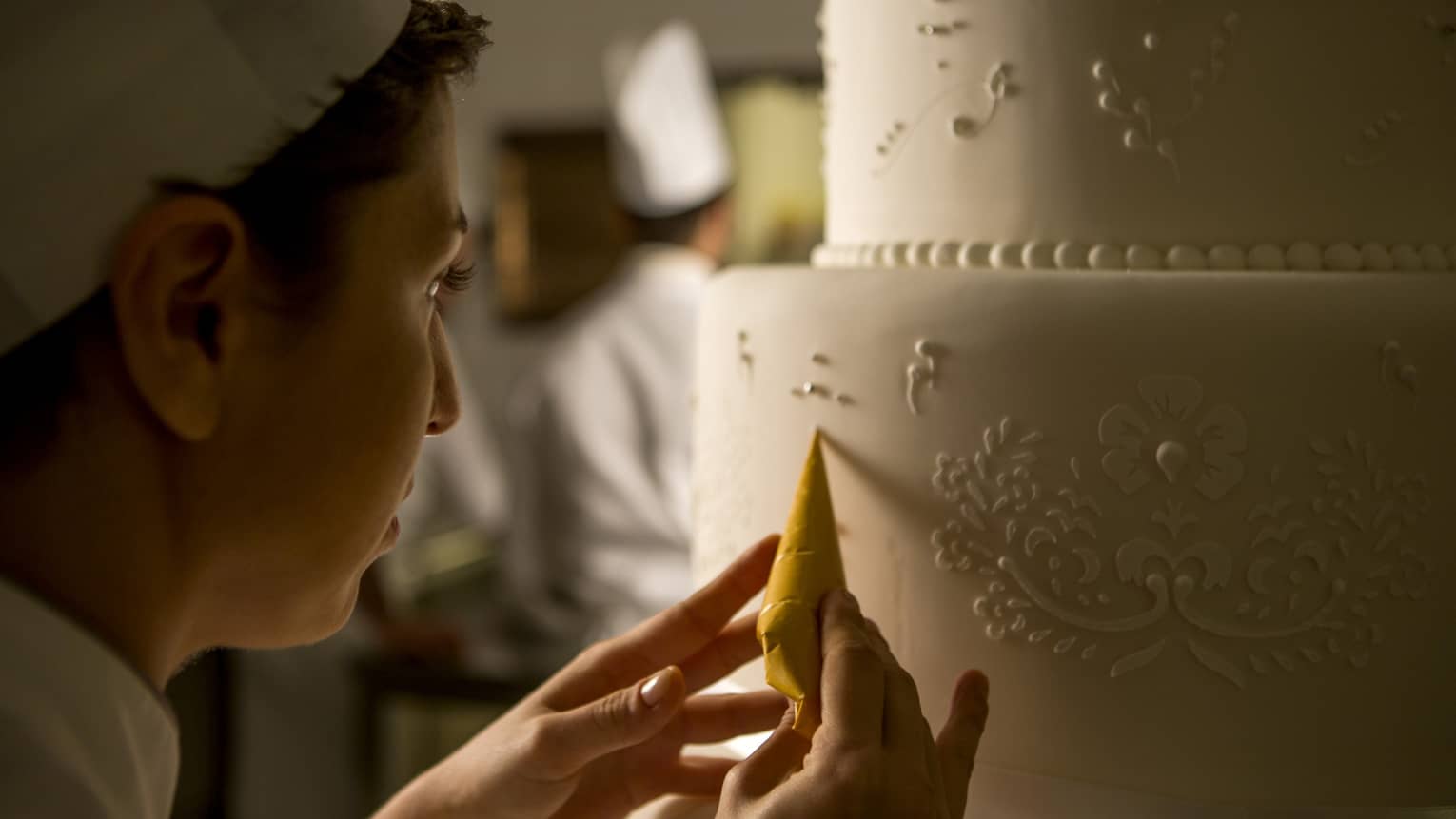 Pastry chef adds decorative details to tiered white wedding cake