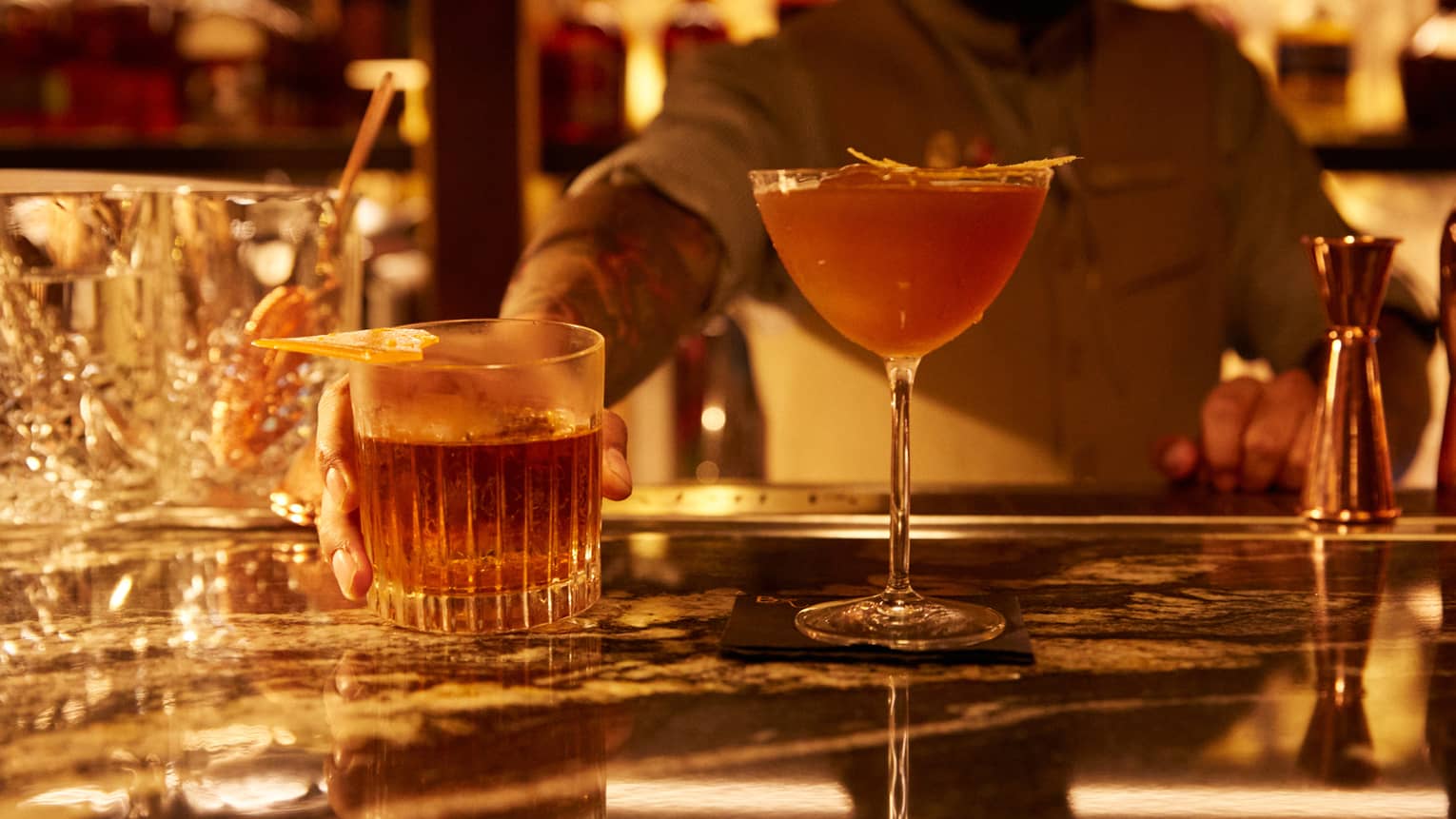 A bartender standing behind cocktail on a counter.