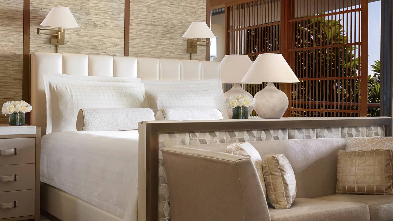 Makai Suite hotel bed, dresser with white flowers, lamp, small plush sofa and silk pillows at foot