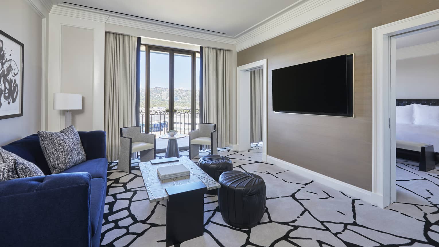 Living room with royal blue sofa, black and white carpet, wall-mountain TV, and an entrance into bedroom