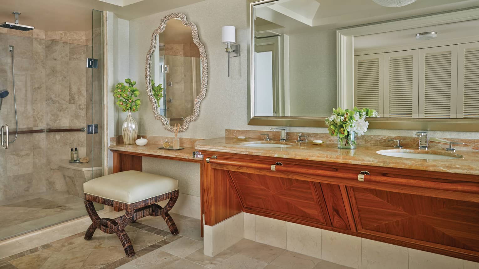Luxury bathroom with dual sinks, marble countertop, glass-enclosed shower and decorative mirror, featuring wood cabinetry