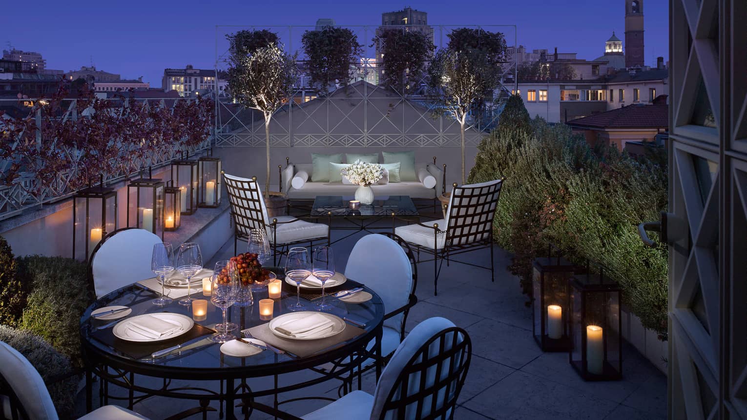 Penthouse Suite lantern-lined rooftop balcony, candle-lit dining table, patio sofa and chairs at night