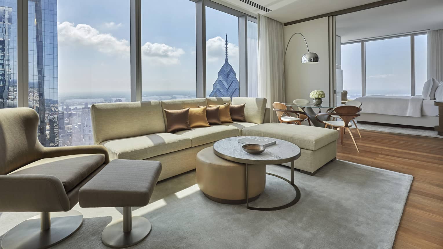 Modern living area with light yellow l-shaped sofa, arm chair, coffee table, Philadelphia city view