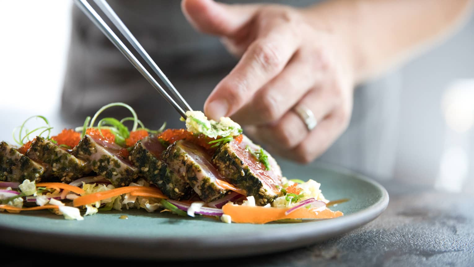 Close-up of chef plating slices of seared tuna on bed of Asian-style coleslaw 