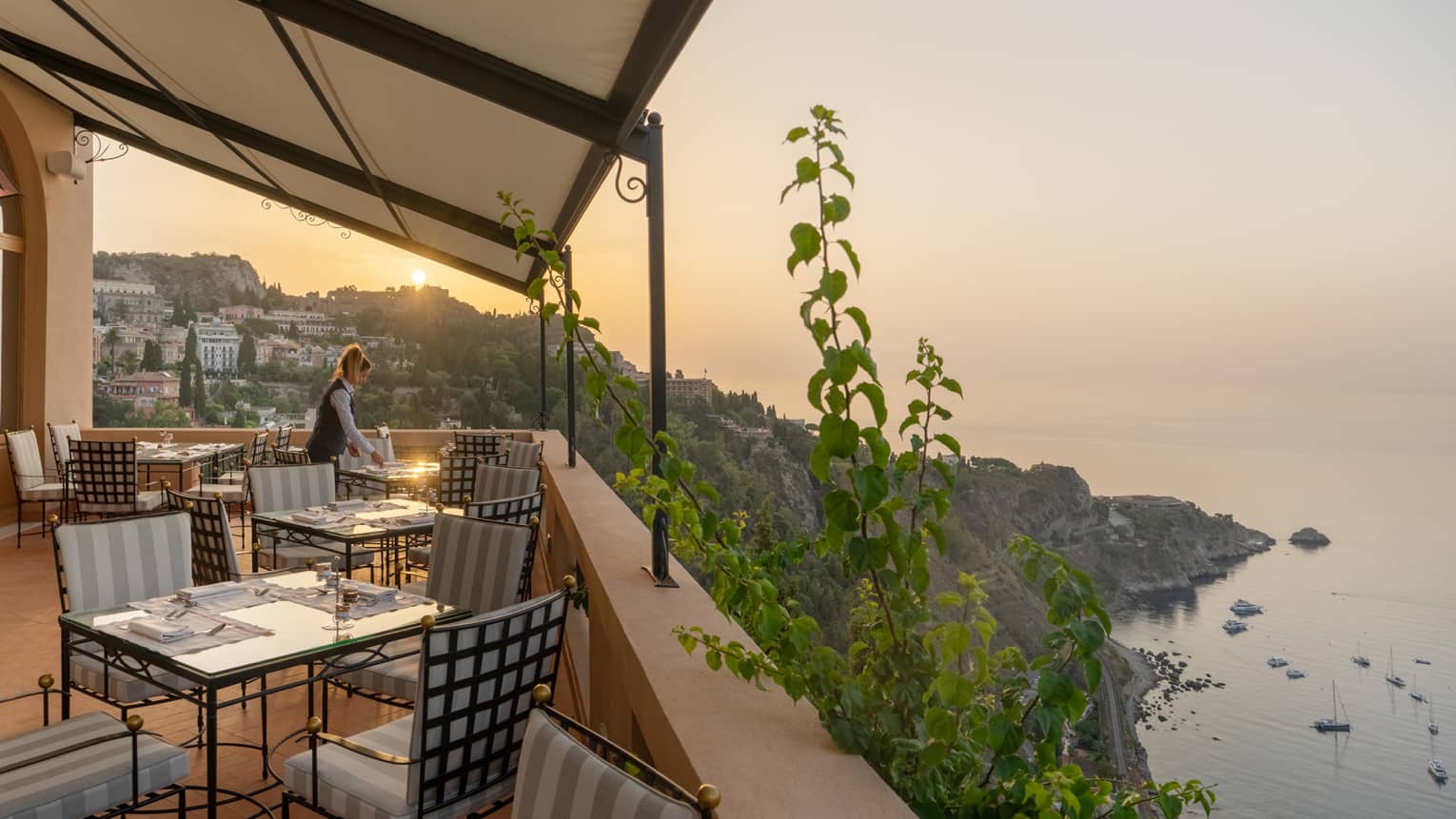 Woman server sets table on restaurant terrace overlooking the sea