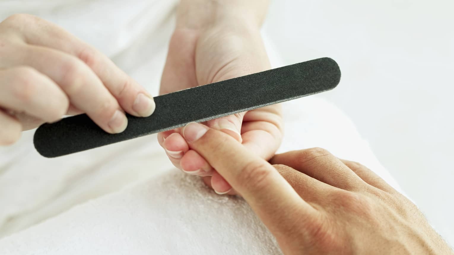 Woman holds manicure nail file to man's fingernails over white towel