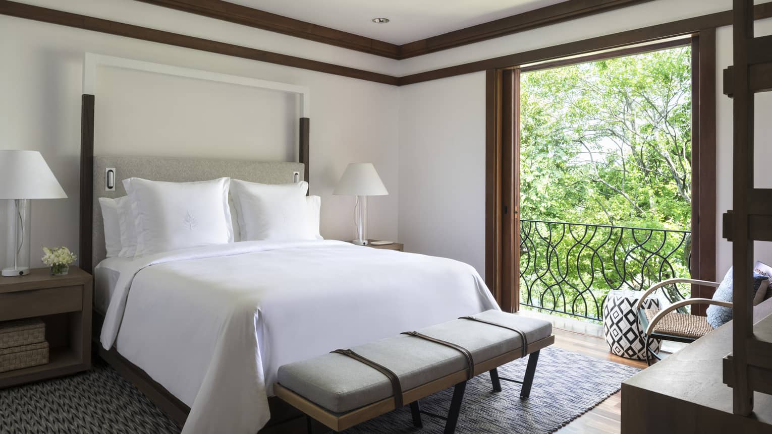 Canopy Suite poster bed with white linens, modern grey bench at foot by open sliding wood doors to sunny terrace