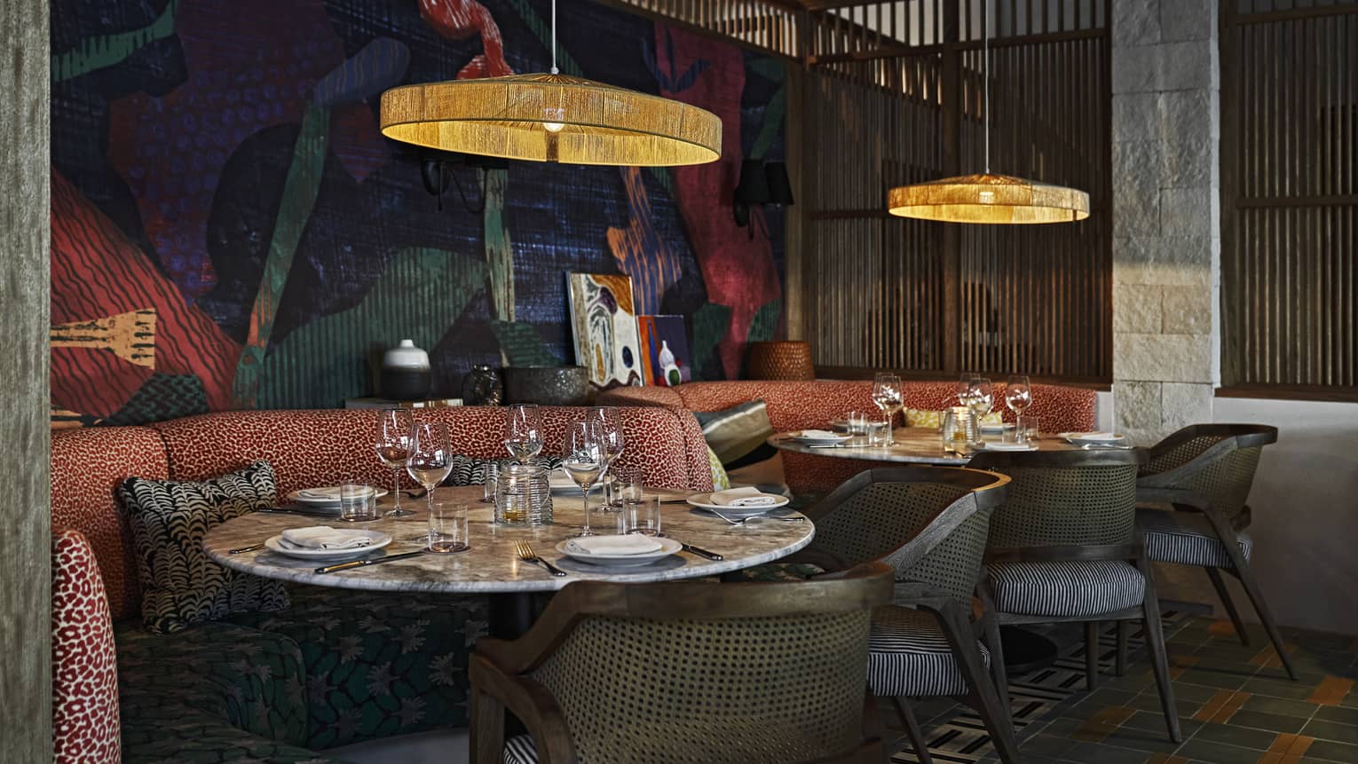An intimate indoor dining space with elegant lighting, upholstered booth and chair seating, round tables and artistic decor