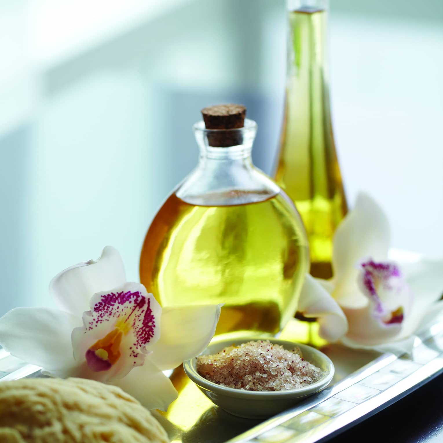 Close-up of small spa bowl with salt scrub, glass bottle with oil, white and purple tropical flower