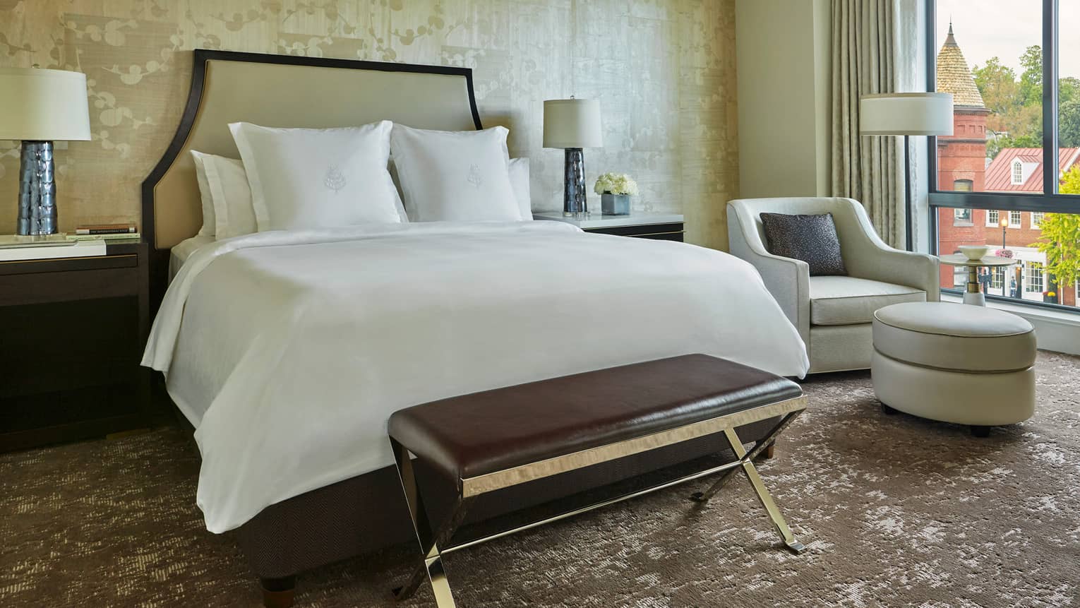 Georgetown suite with leather bench, bed with white linens, headboard against wallpaper, white armchair by sunny window