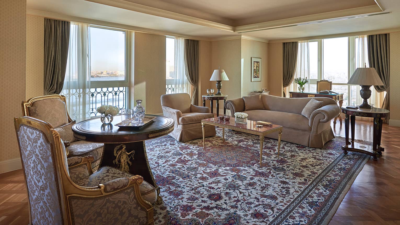 Presidential Suite living room with antique-style armchairs, floral area rug, corner windows