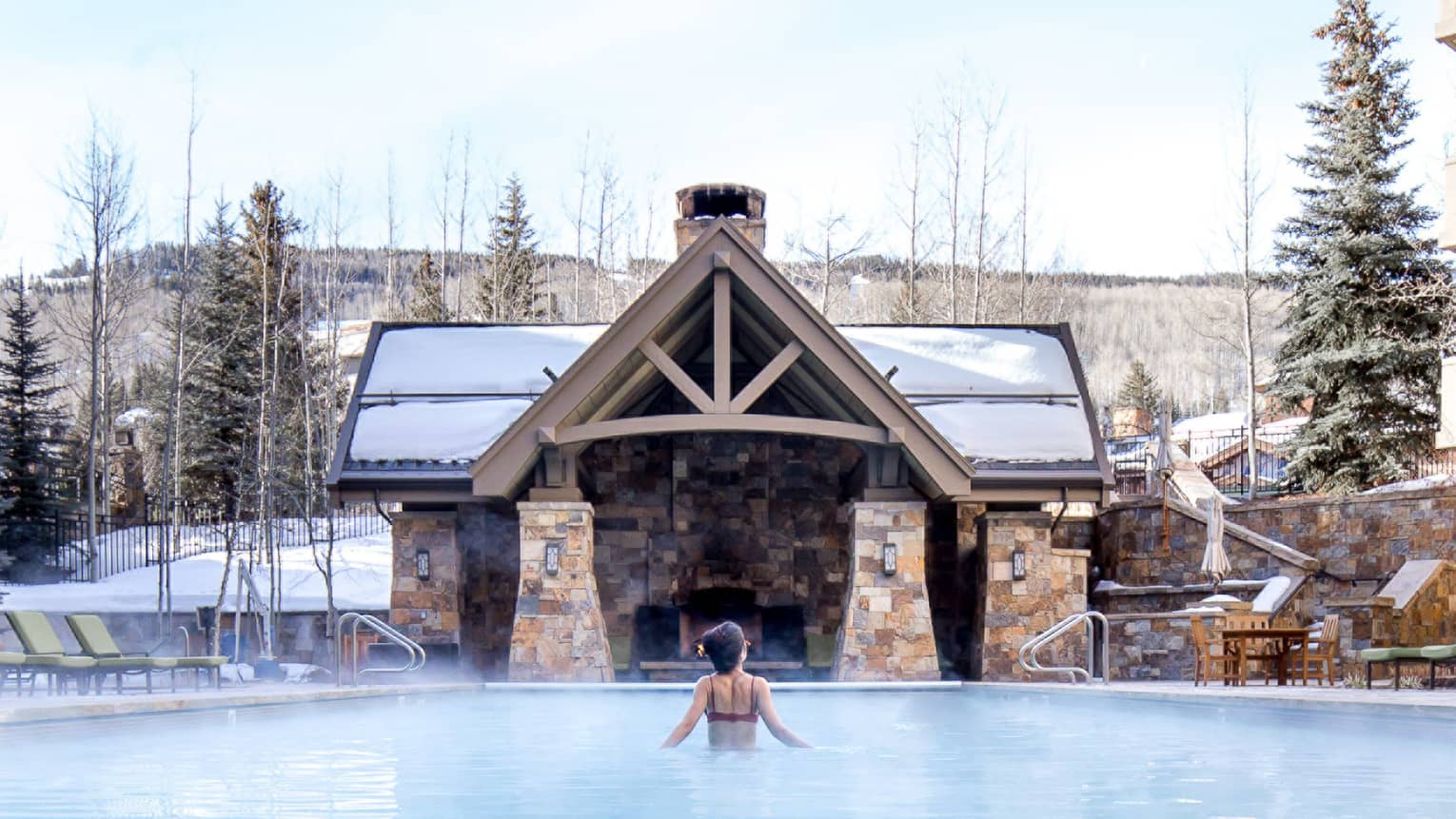 A woman in a pool with trees covered in snow around her.