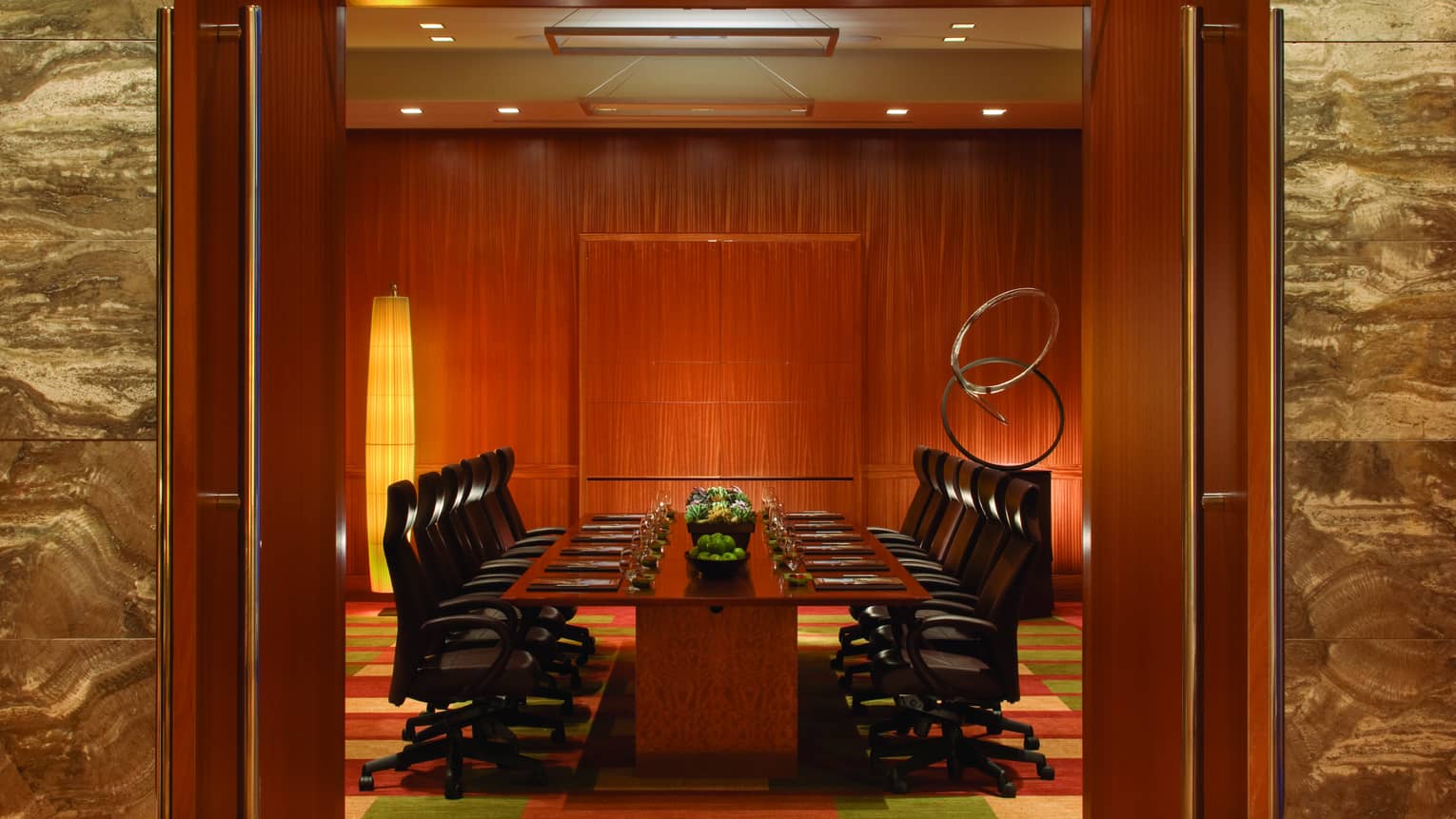 View through wood doors to large boardroom meeting table with black executive swivel chairs