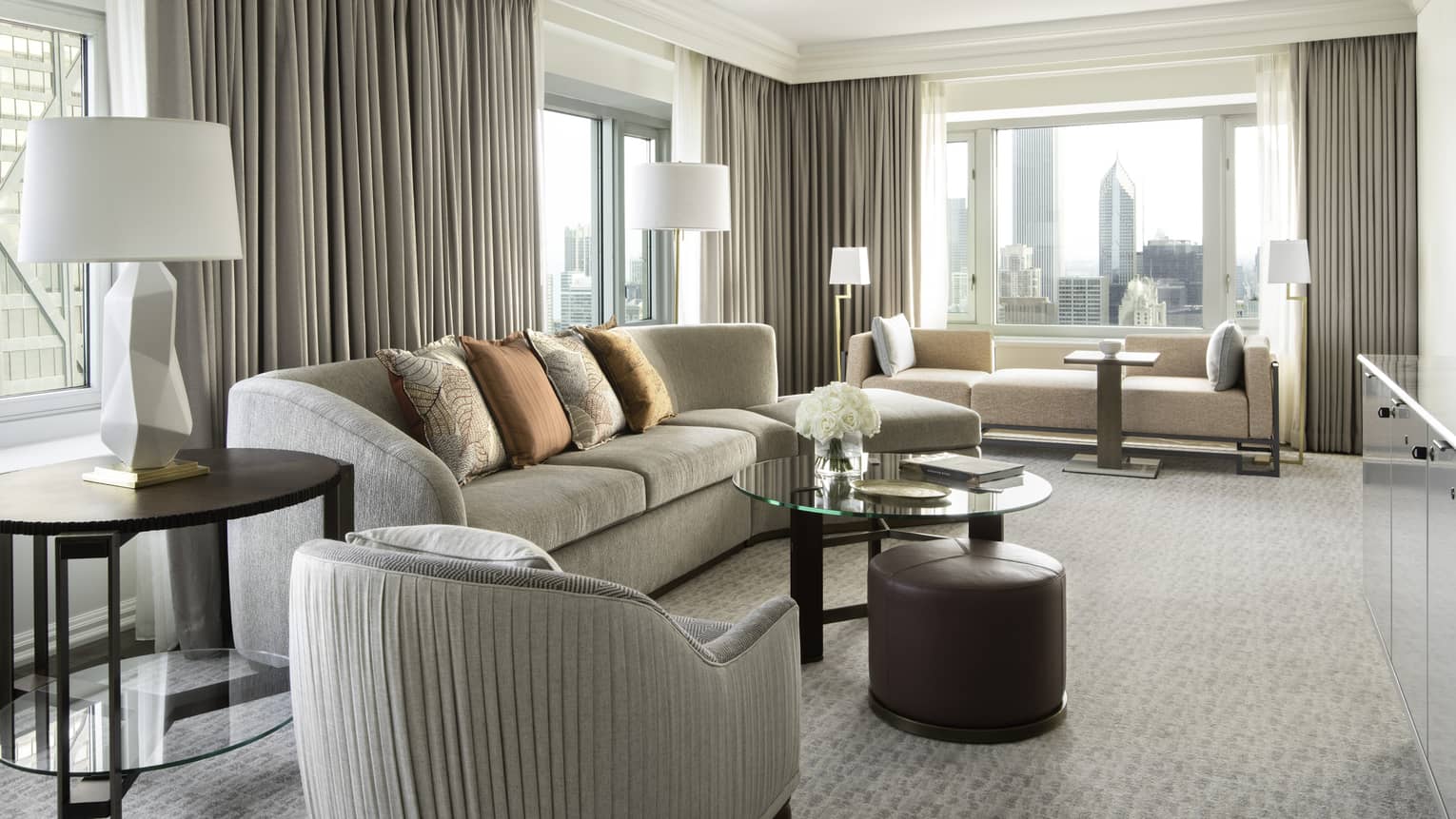 Living area with grey sofa, glass table, beige carpet, grey curtains, large windows