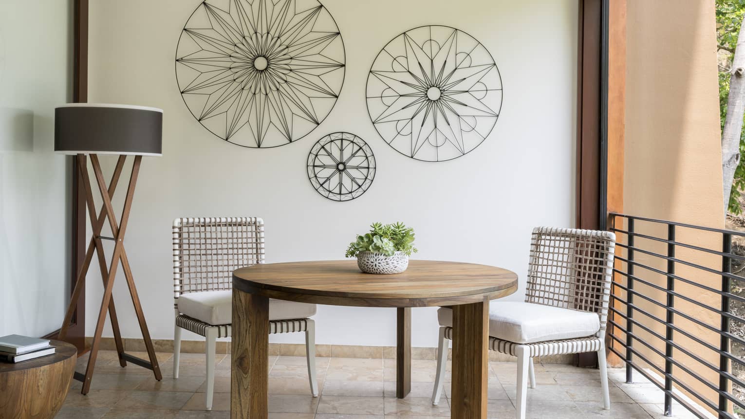 Brisa Room round table with two white wicker chairs on tile terrace, iron decorations on wall